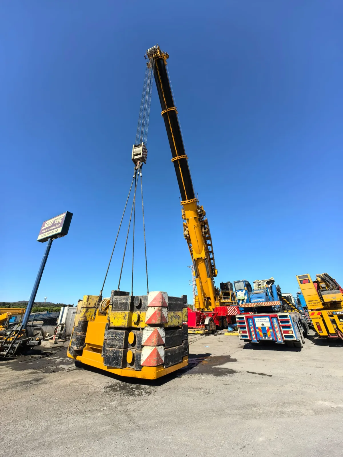 Mobil vinç kancası altında sapanlarla bağlı beton ağırlık bloklarının yakın görünümü