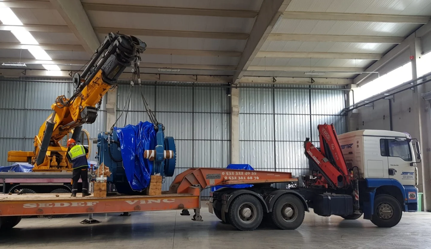 Fabrika içinde makine parçalarının vinçle taşıma aracına yüklenmesi